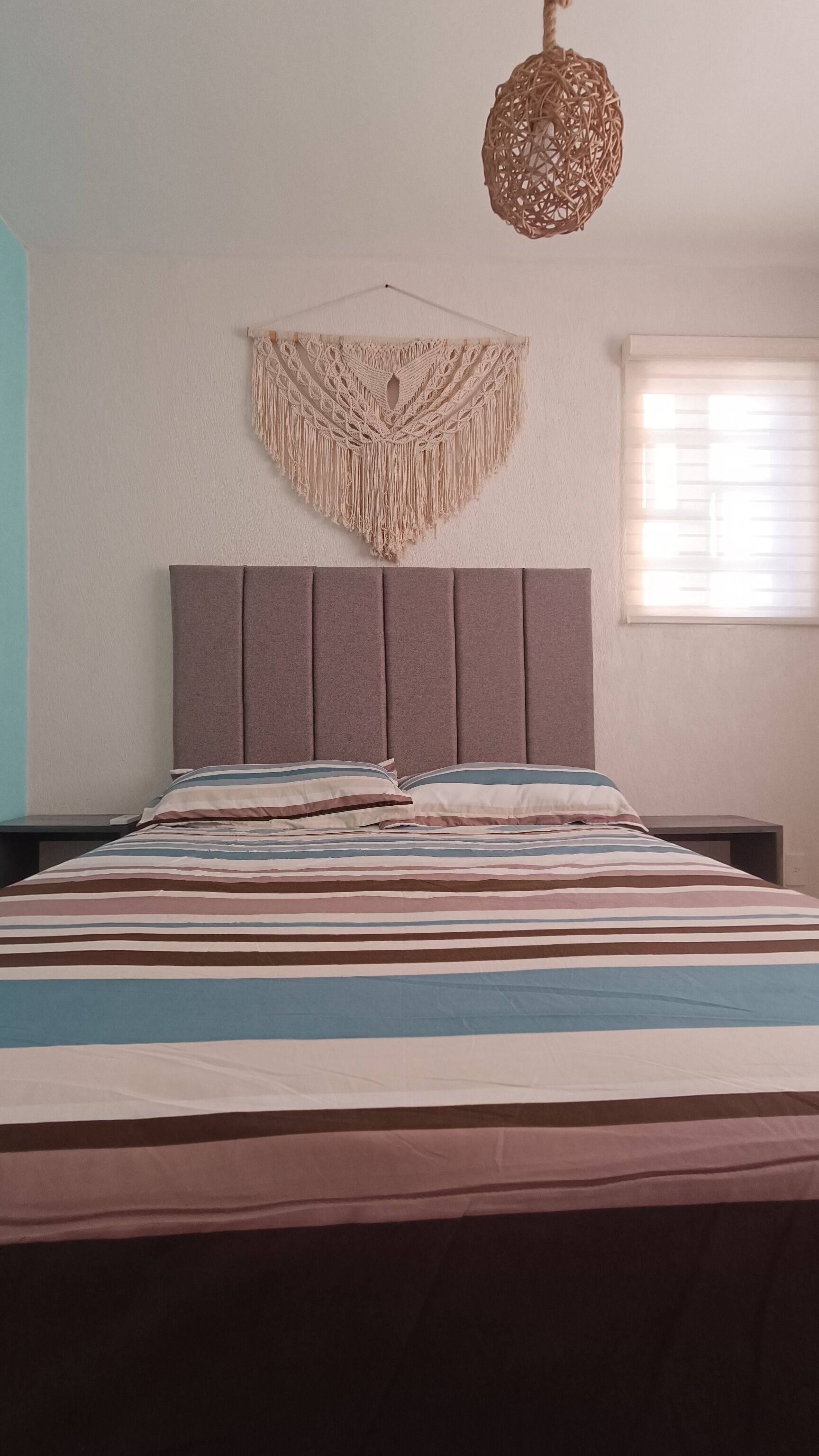 Ein Bett mit gestreifter Bettdecke, ein Wandbehang aus Makramee und eine Pendelleuchte.