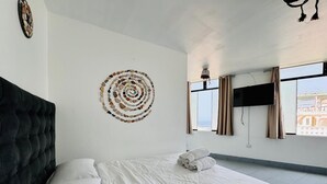 A bedroom with a large bed, a headboard, a wall art piece, a flat-screen TV, and a window with curtains. - Hotel La planicie -Pico Alto (Punta Hermosa)