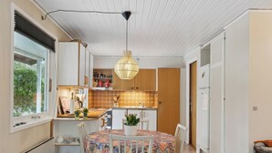 A compact kitchen with a dining area, white cabinetry, a hanging light fixture, and a view through a window. - Cozy summer house by Stevns Klint and Rødvig (Rødvig Stevns)