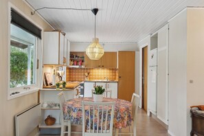A compact kitchen with a dining area, featuring a round table with chairs, a hanging light fixture, and a view of the outdoors through a window. - Cozy summer house by Stevns Klint and Rødvig (Rødvig Stevns)