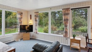 A room with a TV, wooden furniture, and large windows with curtains. - Cozy summer house by Stevns Klint and Rødvig (Rødvig Stevns)