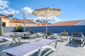 Un salón en la azotea con tumbonas, una mesa y una sombrilla.