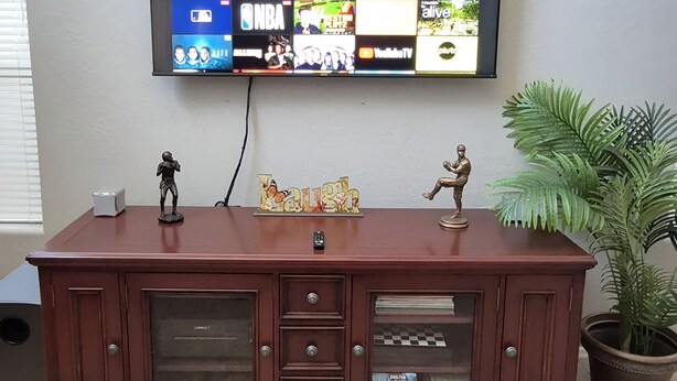 A flat-screen TV mounted on a wall above a wooden entertainment center with two figurines.