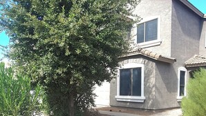 A two-story house with a gravel driveway and a large tree in the front yard.