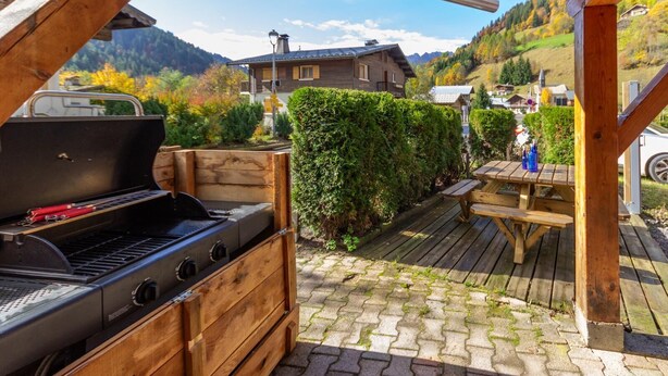 A wooden barbecue grill and picnic table set up on a wooden deck with a mountainous backdrop.