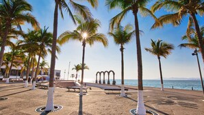 A beachside promenade with palm trees, benches, and a sea view.