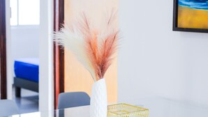 A glass table with a white vase containing pampas grass, a gold tray, and a blue chair in the background.