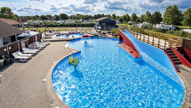 A large outdoor swimming pool with a slide, lounge chairs, and a covered area. - 6 Person Holiday Park Home in Bogense (Bogense)