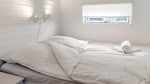 A single-bed room with a white bedspread, a bedside table, and a window with a white blind. - 6 Person Holiday Park Home in Bogense (Bogense)