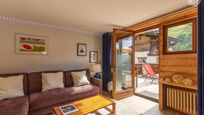 A cozy living room with a brown sofa, a wooden coffee table, and a glass door leading to an outdoor seating area. - La Duchere - 1st Floor (LA GIETTAZ)