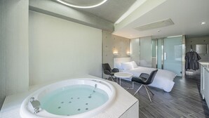 A modern hotel room with a large bathtub, a sofa, and a small table.