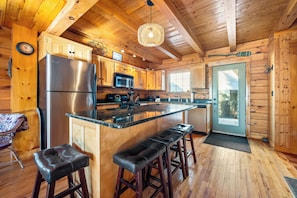 A wooden cabin kitchen with a stainless steel refrigerator, microwave, and bar stools.