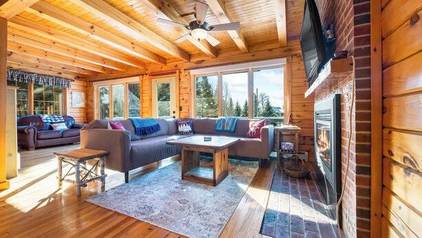 L’intérieur chaleureux d’un chalet avec un plafond en bois, une cheminée, un ensemble de canapés et un téléviseur fixé au mur.