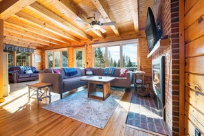 A cozy cabin interior with a wooden ceiling, a fireplace, a sofa set, and a television mounted on the wall. - 3 Summit Road, shared waterfront on Rangeley Lake (Rangeley)