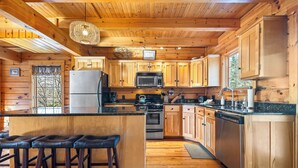 Une cuisine rustique, située dans une cabane en bois, avec un îlot central, des tabourets de bar et une grande fenêtre.
