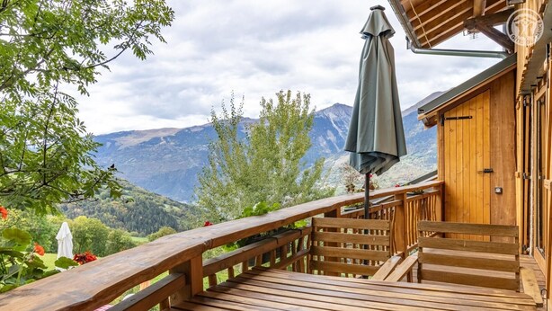 Une terrasse en bois avec un banc et un parasol, offrant une vue sur un paysage montagneux.