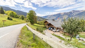 Une cabane de montagne avec un toit en métal, des voitures garées et une clôture en bois le long d’une route.