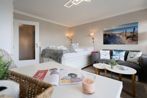 Una habitación de hotel moderna con una cama, un sofá, una mesita con una bebida y un cuadro de una playa.