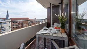 A balcony with a table set for two, a potted plant, and a view of buildings in the background. - Küstenmuschel - Modern 1-room apartment, close to the beach, balcony, WLAN. Pets (Westerland)
