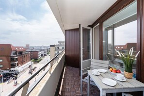 Un balcón con mesa lista para comer, con vistas a una calle con edificios y gente.
