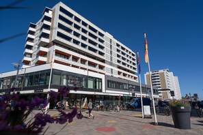 Un hotel de varios pisos con diseño moderno, que cuenta con balcones y un espacio comercial en la planta baja.