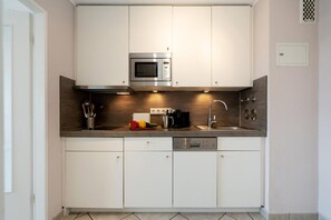 Een moderne keuken met witte kasten, een roestvrijstalen magnetron, een koffiezetapparaat en een vaatwasser.