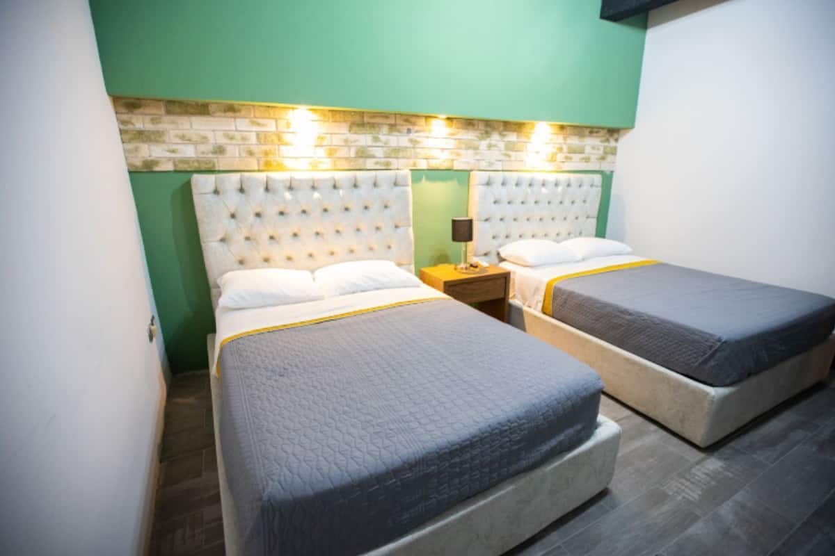 A room with two beds, each with a headboard and a bedside table with a lamp.