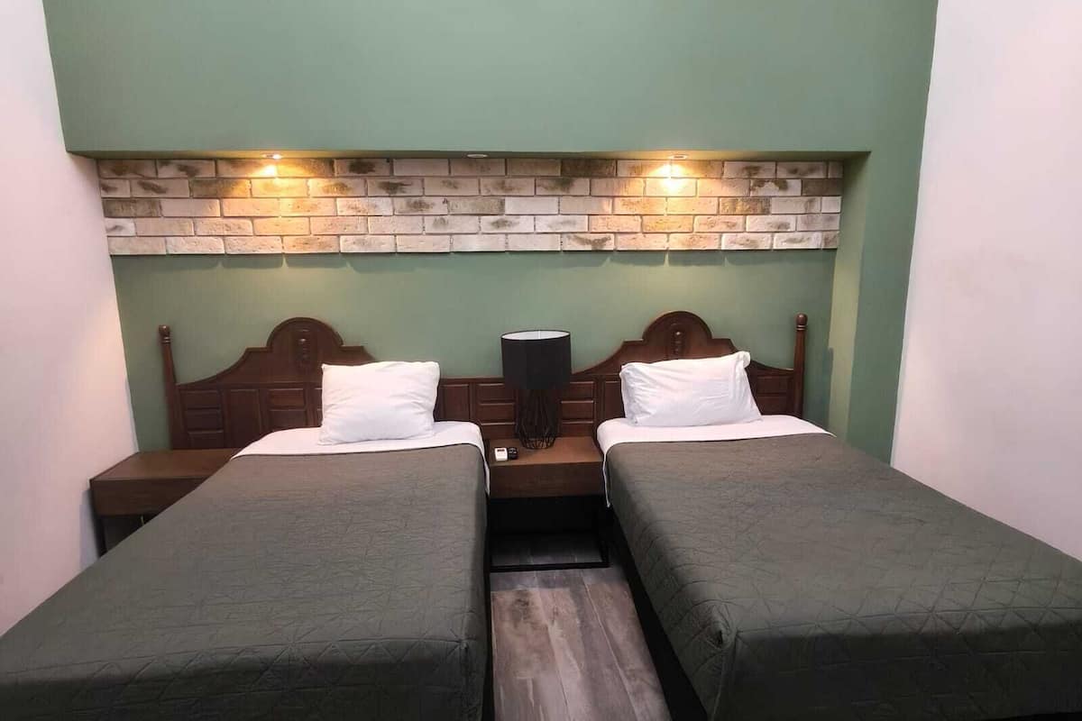 A room with two beds, a brick wall, and a nightstand with a lamp.
