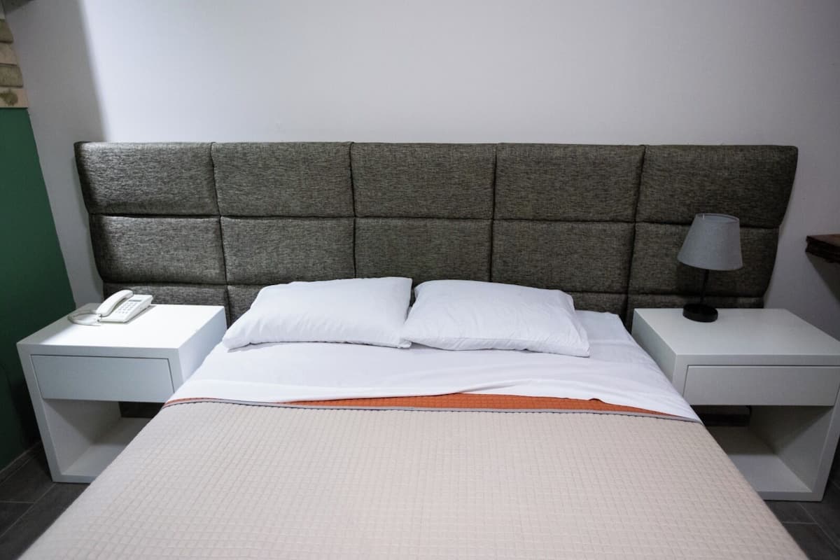 A hotel room with a bed, two bedside tables, a lamp, and a phone on one table.