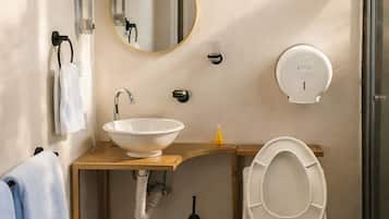 Un baño con lavamanos, espejo, inodoro y cubo de basura.