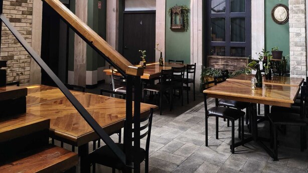 Un ristorante con una scala, tavoli in legno e piante pensili.