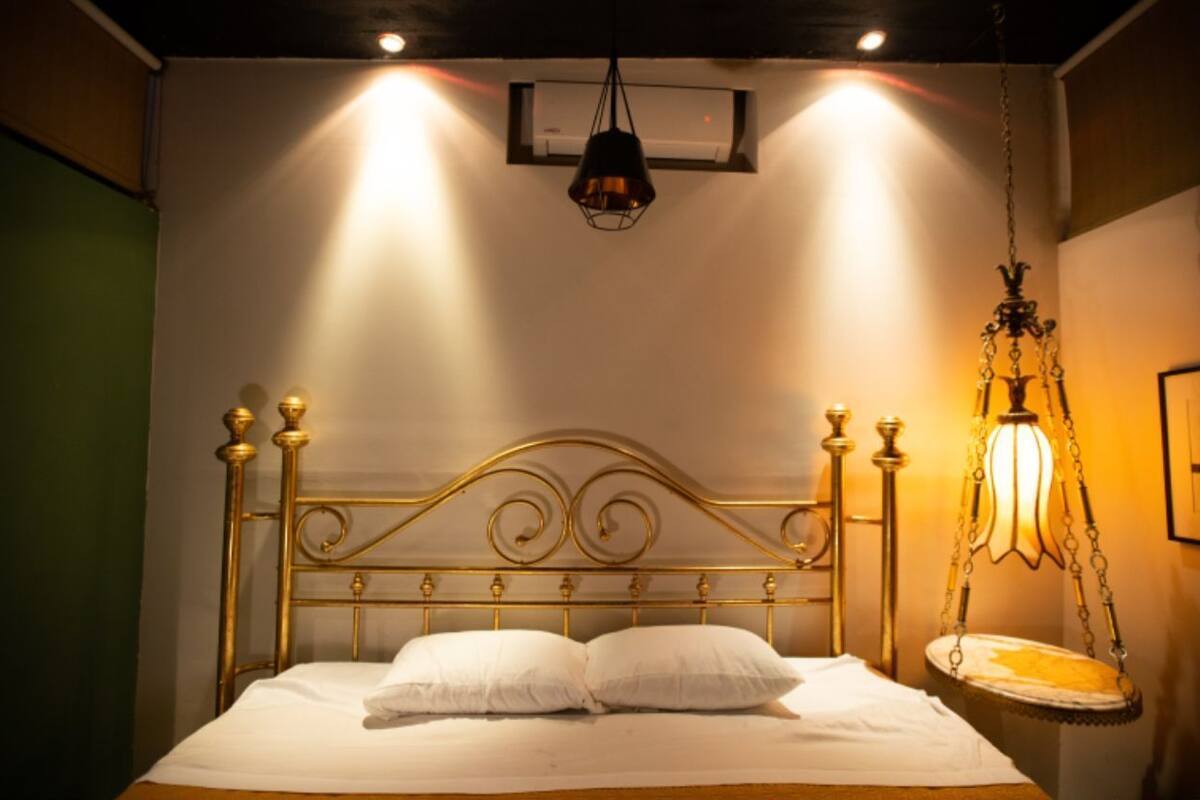 A bed with a gold headboard, white bedding, and a hanging light fixture.