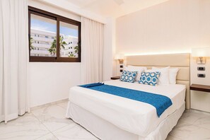 A hotel room with a large bed, a nightstand, a window with curtains, and a view of palm trees. - Aqua Joy | 3BR Family Swim-Up + Whirlpool (Bavaro)