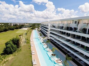Een hotel met een lang zwembad, meerdere balkons en een weelderig groen landschap.