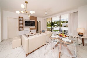 A modern living room with a sofa, glass dining table, and a TV mounted on the wall. - Aqua Joy | 3BR Family Swim-Up + Whirlpool (Bavaro)