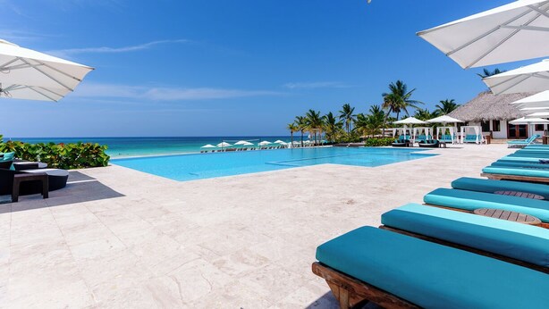 A poolside area with lounge chairs and umbrellas, a clear blue sky, and a view of the ocean. - Directo piscina jardín terraza @ Cana Rock (Bavaro)