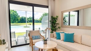 A modern living room with a sofa, a chair, a small table, and a view of a pool and greenery outside. - Directo piscina jardín terraza @ Cana Rock (Bavaro)