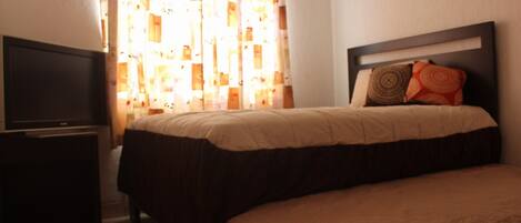 A hotel room with a bed, a TV, and a window with patterned curtains.