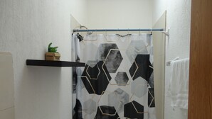 Une salle de bain avec un rideau de douche orné d’un motif géométrique, des toilettes, une étagère avec une plante et une serviette accrochée au mur.