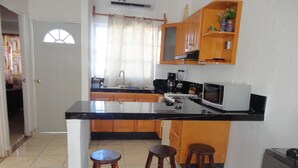 Une cuisine avec des meubles de rangement en bois, un plan de travail noir, un évier, une cuisinière et deux tabourets.