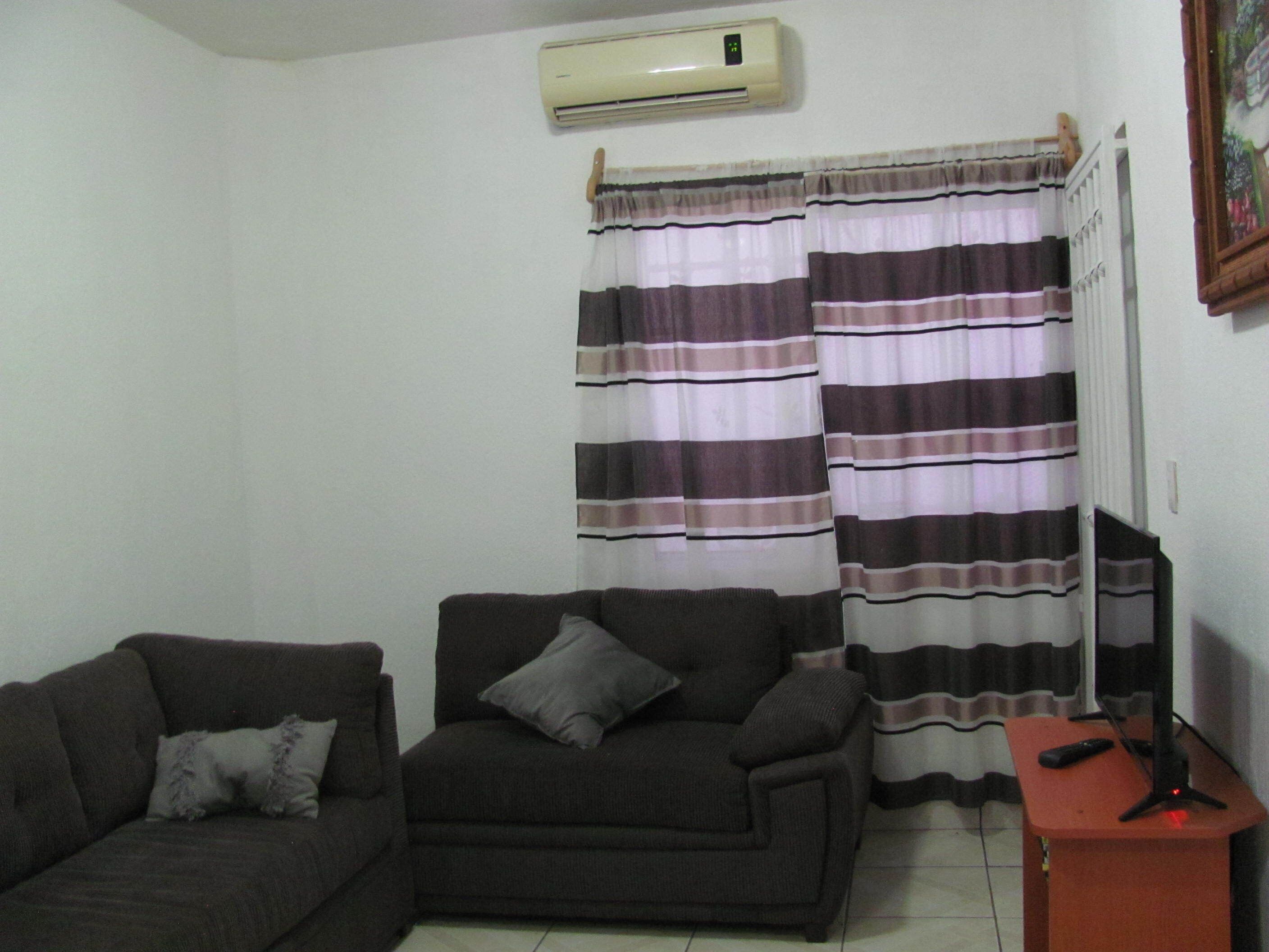 Una sala de estar con sofá, sillón, mesita y cortina.