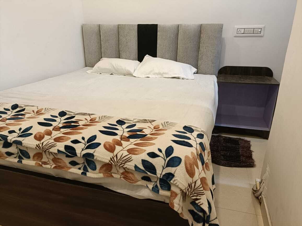 Ein Bett mit einer blumigen Tagesdecke, einem grau gepolsterten Kopfteil und einem weißen Kissen.