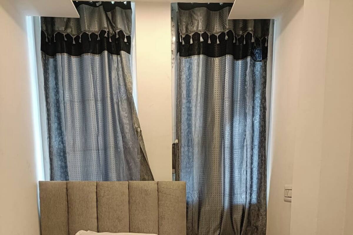 Ein Schlafzimmer mit einem Bett, einem Nachttisch, einem Schreibtisch und Vorhängen.