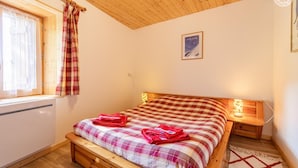 Une chambre avec un lit en bois, une fenêtre avec des rideaux, une table de chevet avec une lampe et une affiche accrochée au mur.