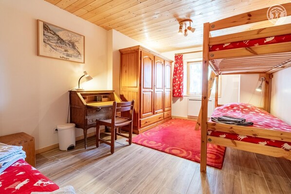 A cozy room with a bunk bed, a wooden desk with a chair, a radiator, and a window with curtains.