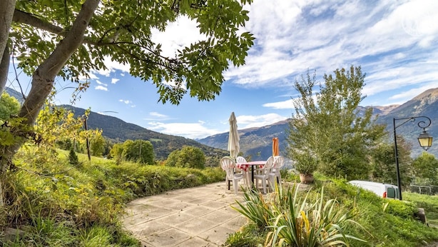 Une terrasse dallée avec des sièges extérieurs, entourée d’une végétation luxuriante et offrant une vue sur un paysage montagneux.