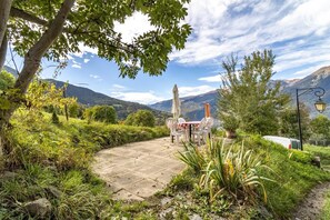 Une terrasse dallée avec des sièges extérieurs, entourée d’une végétation luxuriante et offrant une vue sur un paysage montagneux.