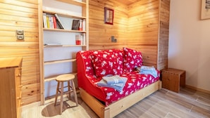 Une pièce chaleureuse avec un mur en bois, un canapé rouge agrémenté de coussins à motifs, un petit tabouret et une bibliothèque.