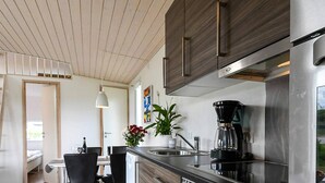 A modern kitchen with stainless steel appliances, a dining area with black chairs, and a wooden ceiling. - 6 Person Holiday Park Home in Asperup (Middelfart)