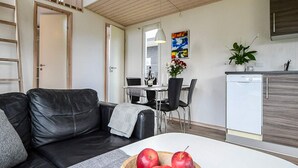 A modern living room with a black leather sofa, a dining area with a table and chairs, and a kitchen area with a dishwasher and cabinets. - 6 Person Holiday Park Home in Asperup (Middelfart)